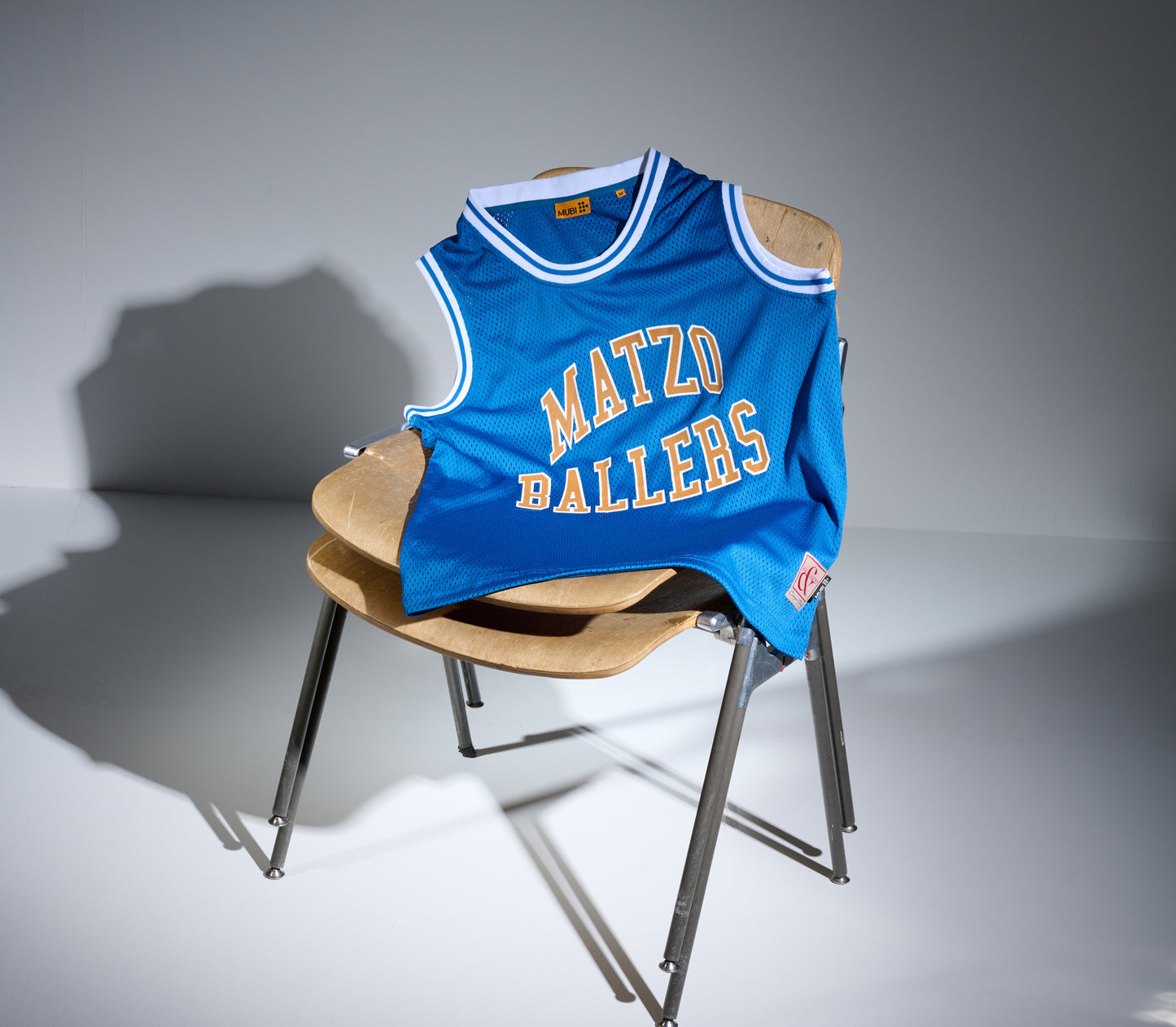 Blue basketball jersey with 'Matzo Ballers' text on a wooden chair against a gray background